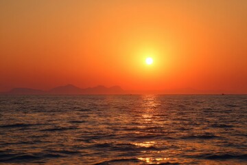 Obraz premium Vibrant orange sunset over calm ocean waves with distant mountains