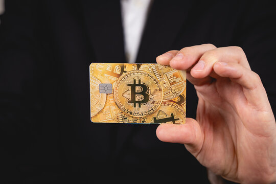 Une personne en costume tenant une carte bancaire pour d&eacute;penser ses cryptomonnaies bitcoin.