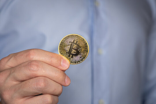 Gros plan sur une personne tenant avec sa main une pi&egrave;ce symbolisant le bitcoin. En arri&egrave;re plan, elle est habill&eacute;e d'une chemise.