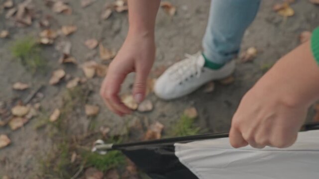 Camper securing tent corner during camping, hands inserting pole end into grommet and fabric sleeve, ground scattered with autumn leaves, white sneakers and jeans visible, closeup shots of tensioning