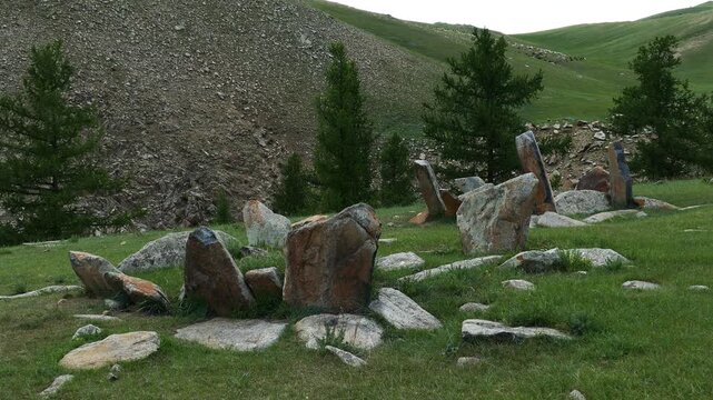 Stone slabs of ancient burial structures (Kheregsuurs) in the Mongolian steppe on the background rocky mountain. Summer sunny evening.  Landscape of Mongolia.