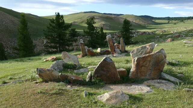 Stone slabs of ancient burial structures (Kheregsuurs) in the Mongolian steppe on the background rocky mountain. Summer sunny evening.  Landscape of Mongolia.