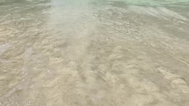 Sea waves washing white pristine sand filmed at wave level, tropical beach close-up nature background.