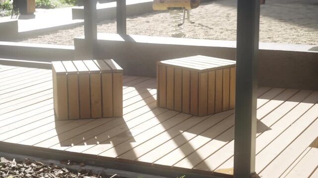 Rustic wooden sitting blocks rest on durable timber decking near sandy playground. Cozy rest area provides parental supervision spot