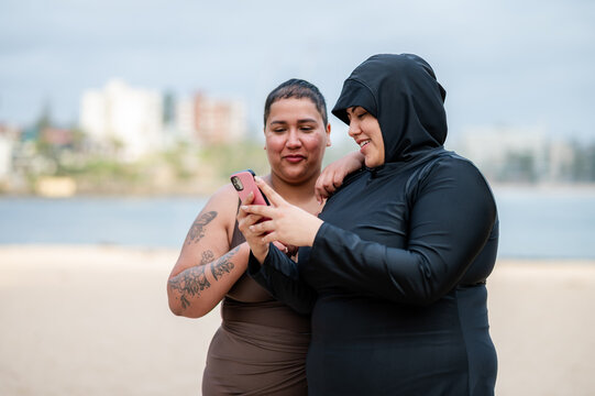 Multiracial women checking their phone on the sandy shore at the beach