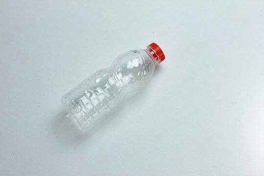Clear plastic bottle with red cap lies on plain white surface. Simple, clean background highlights bottle's shape and texture. Minimalist composition suits product or recycling themes