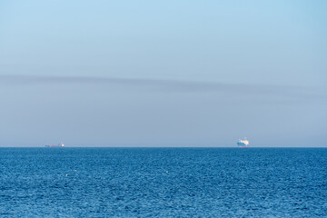 Fototapeta premium Two cargo ships sail on the vast blue sea under a clear sky