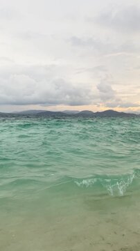 Azure ocean waves at sunset on a tropical Thai coastline, vertical video of peaceful sea nature landscape.