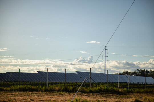 Expansive solar panel array under a vast sky with power lines and clouds