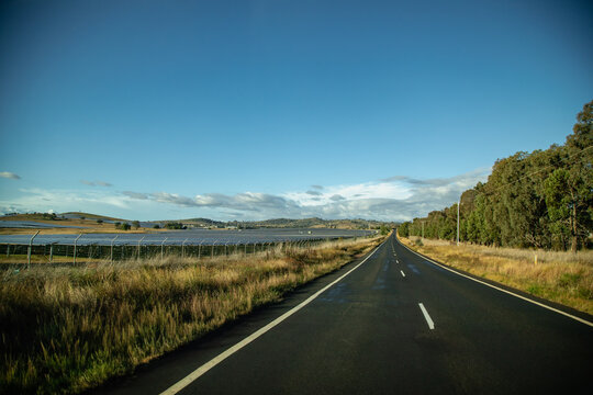 Long open road passing by solar farm under a vast blue sky with scattered clouds