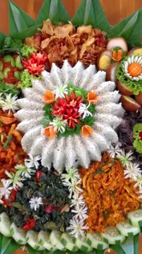 A vibrant and detailed top-down view of Indonesian Tumpeng Nasi Daun Jeruk (Lime Leaf Rice) surrounded by traditional side dishes, decorated with beautiful vegetable carvings and garnishes