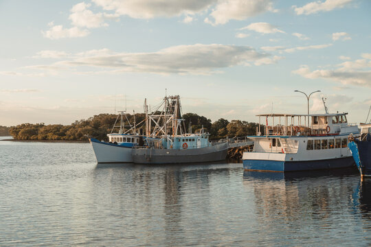 Fishing boats and a passenger ferry docked in a calm harbour at sunset