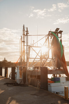 Fishing trawler docked at pier during golden hour with sun flare and nets
