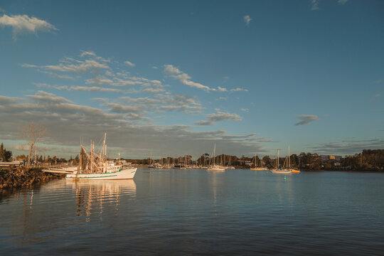 Serene harbour at sunset with fishing boats and sailboats docked under a cloudy sky