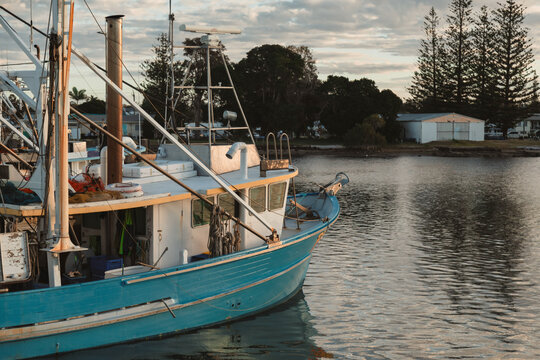 Blue fishing trawler docked in calm water at sunrise with coastal buildings in background