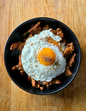 A Bullseye egg ior a Sunny-side-up fried egg on a black bowl with fried meat and rice. A mixture of a Sri Lankan and Chinese style fusion food