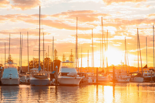 Golden hour glow at sunset over a marina filled with sailboats and yachts reflecting on the water