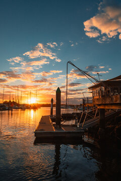Golden sunset over a tranquil marina with docked sailboats, wooden pier and bollards