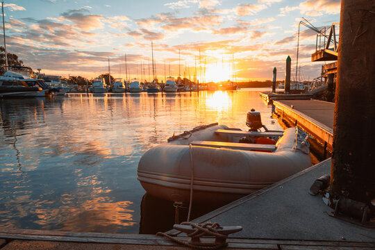 Golden sunset over a marina with boats docked and a small inflatable dinghy in the foreground