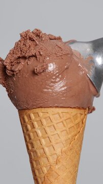 4k vertical video Chocolate ice cream scoop in waffle cone with spoon taking bite Close-up creamy texture and rich brown tone, ideal for dessert food concept product advertising and summer refreshment