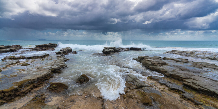 Low angled view of rough waves washing over rock ledges under a dark stormy sky