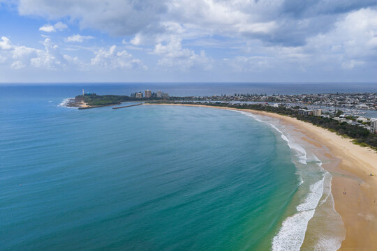 Aerial view of a long curved beach stretching to a coastal headland and calm blue bay