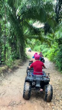 Tourist riding ATV through tropical mud trail in Thailand, vertical video of offroad quad bike adventure activity.