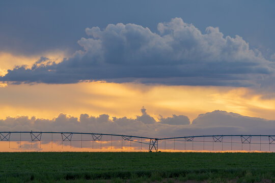 A dramatic sunset sky behind a large farm irrigation sprinkler