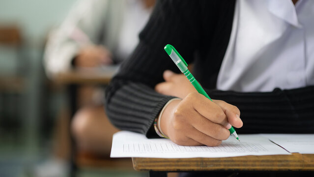 Close-up of Student Hand Using Green Pen to Mark Answer Sheet in Classroom