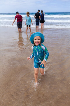 Happy young child running away from ocean waves with family behind in the surf