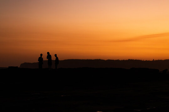 Golden sunset sky above three silhouetted teens talking together standing on coast