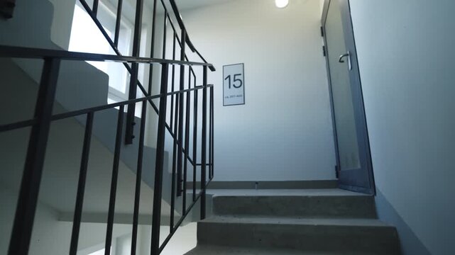 Information sign with floor and apartments numbers on wall of staircase. Empty steps with metal railings inside modern multistory building