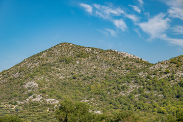 Fototapeta premium Rocky green hillside under blue sky with wispy clouds