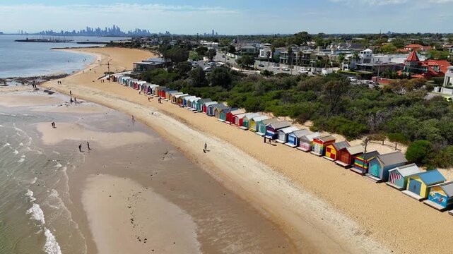 Aerial drone view of Brighton Beach, Port Phillip Bay, Melbourne, Victoria. Colorful Brighton Bathing Boxes along the beach. Tourists walking on the sand near wooden beach huts.