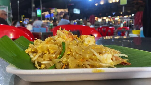 Close-up of Pad Thai noodles on a plate at a Thai night street market, golden stir-fried noodle dish.