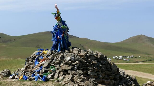 A sacred pile of stones (ovoo, obo) against the background of low hills and blue sky. Yurts in distance. The Mongolian landscape. Summer sunny  day.
