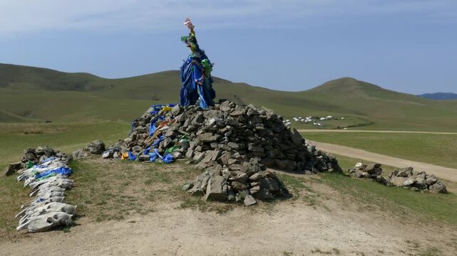 A sacred pile of stones (ovoo, obo) against the background of low hills and blue sky. Yurts in distance. The Mongolian landscape. Summer sunny  day.
