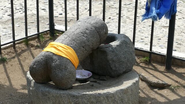 A large stone sculpture of a phallus, tied with a yellow silk scarf behind an iron fence. Karakorum phallus, a summer sunny day. Kharkhorin, Mongolia.
