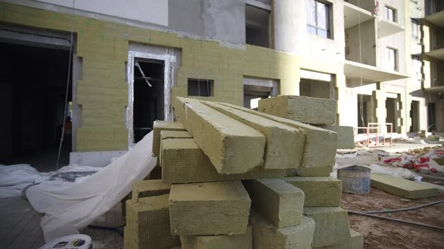 Wooden beams stack placed near incomplete multistorey building. Sustainable materials pile on ground at construction site. Urban development