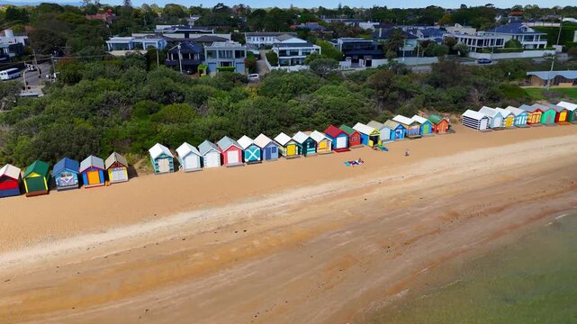 Aerial drone view of Brighton Beach, Port Phillip Bay, Melbourne, Victoria. Colorful Brighton Bathing Boxes along the beach. Tourists walking on the sand near wooden beach huts. 