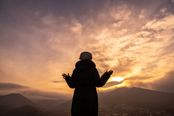 Fototapeta premium Woman sunset silhouette stands on mountain with arms open toward dramatic golden sky
