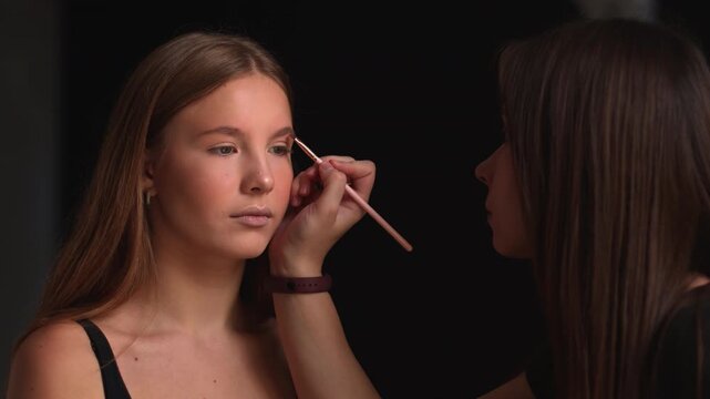 Makeup artist applying eyebrow powder using an angled brush on a young beautiful model in a beauty salon, a professional visagist correcting the shape of the eyebrows