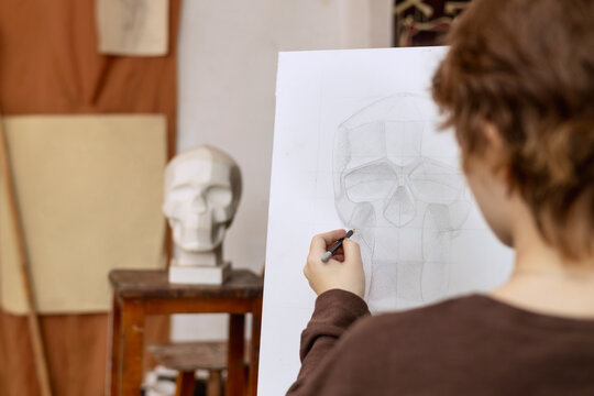 A female artist paints a human skull from a plaster cast. Real photo of an art studio.