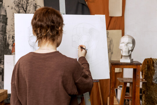 A female artist paints a human skull from a plaster cast. Real photo of an art studio.