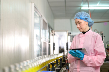 Female quality control inspector checking bottled fruit juice on production line in beverage factory, using tablet for monitoring and inspection.