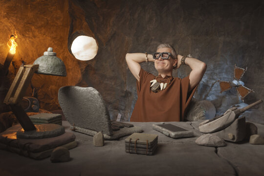 Prehistoric Success: Funny Caveman Relaxing and Feeling Good at His Modern Stone Desk
