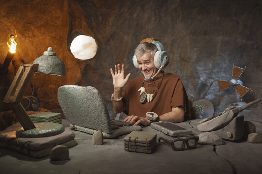 Prehistoric Videoconference: Funny Caveman Waving on a Stone Laptop Video Call in a Cave Office