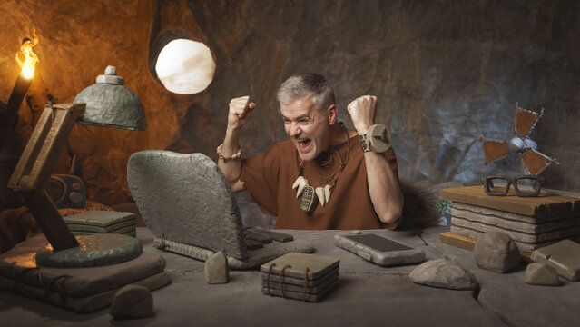 Prehistoric Success: Funny Caveman Celebrating Victory at His Modern Stone Laptop Desk