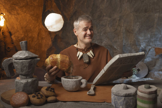 Prehistoric Morning News: Funny Caveman Reading Stone Newspaper During Breakfast in a Cave