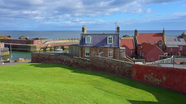 H&auml;user mit Meerblick, umgeben von gr&uuml;ner Wiese und einer Ziegelmauer unter blauem Himmel, Dunbar, East Lothian, Schottland, Vereinigtes K&ouml;nigreich, Gro&szlig;britannien